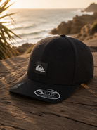 Gorra Quiksilver Adapted Black Flexfit Tech hombre estilo surf premium junto al mar al atardecer