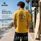 Camiseta Rip Curl Search Icon Mustard Gold para hombre en fotografía editorial propia de THE SURF TOWN PREMIUM SURF SHOP con escenario surf lifestyle junto al mar.