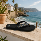 Sandalias Reef Baja Elana Black Frosty para mujer sobre piedra junto al mar en cala mediterránea con estilo beach lifestyle premium y ambiente Costa del Sol