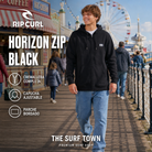 Hombre con sudadera Rip Curl Horizon Zip Black en un muelle vacacional, imagen editorial propia de THE SURF TOWN