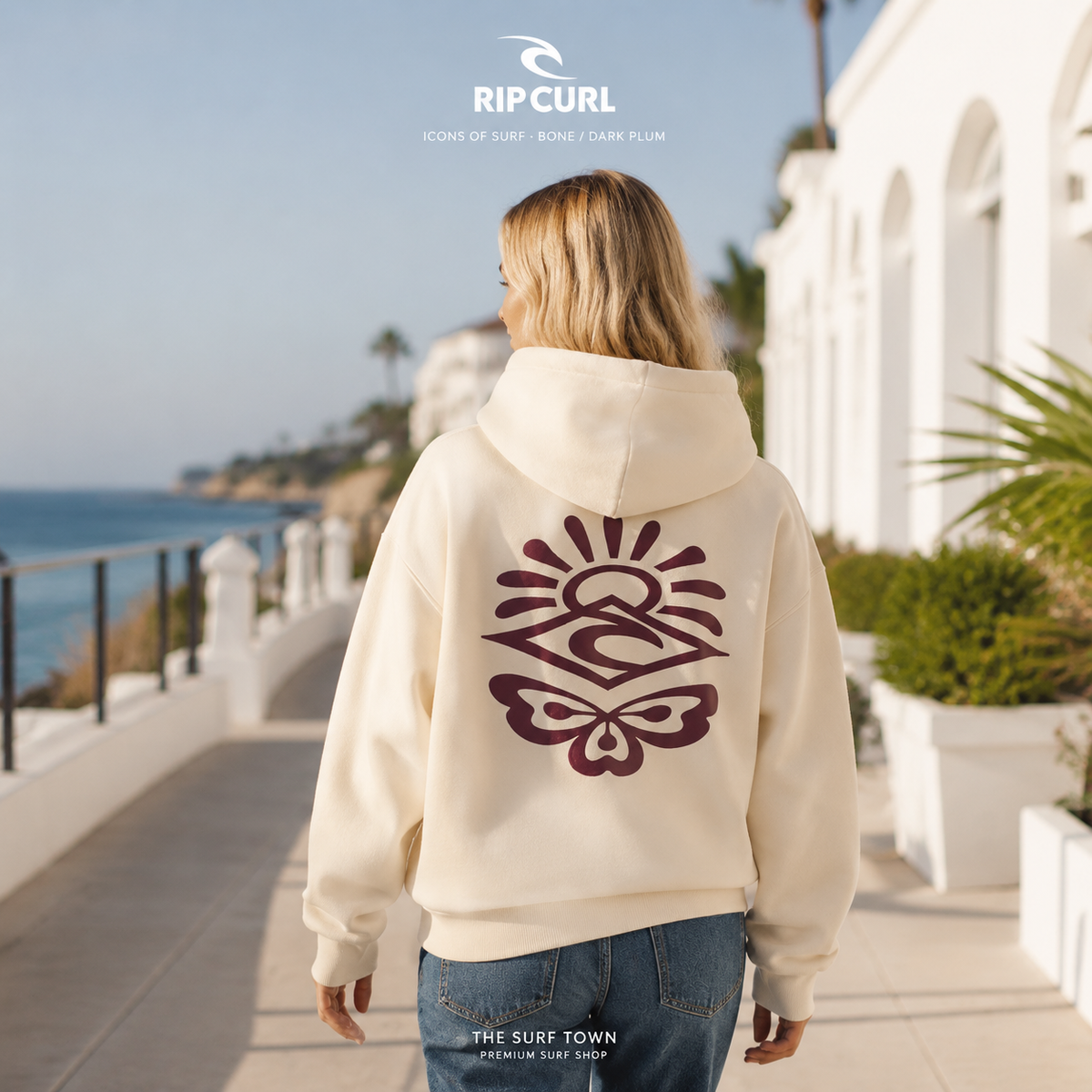 Sudadera Rip Curl Icons of Surf Bone/Dark Plum para mujer, vista trasera en un paseo costero premium, imagen editorial propia de THE SURF TOWN.