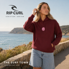 Sudadera Rip Curl Icons of Surf Dark Plum para mujer con capucha y gráfico rosa, en un mirador frente al océano, imagen editorial propia de THE SURF TOWN.