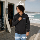 Sudadera Rip Curl Made For Zip Washed Black para hombre junto a una furgoneta de surf frente al océano, imagen editorial propia de THE SURF TOWN