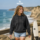 Sudadera Rip Curl Varsity Washed Black para mujer en un mirador costero después de surfear, imagen editorial propia de THE SURF TOWN