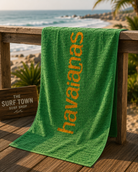 Toalla Havaianas verde y amarilla en ambiente surf lifestyle premium frente al mar
