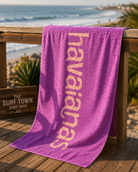 Toalla Havaianas morada coral de playa en ambiente surf lifestyle premium frente al mar