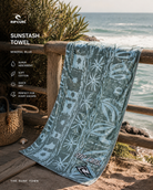 Toalla Rip Curl Sunstash Mineral Blue en escena coastal lifestyle premium junto al mar