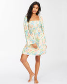 Vestido corto con mangas largas acampanadas estilo boho de estampado de flores tropicales en tonos pastel. Corte imperio con elástico, tejido arrugado fluido de viscosa.